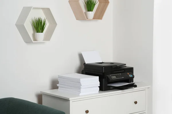 Modern printer and paper sheets on white chest of drawers indoors