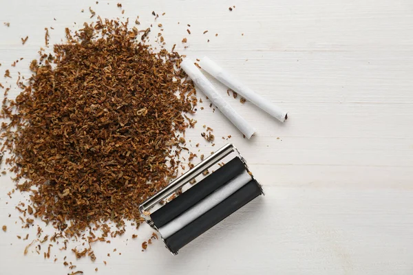 stock image Roller, tobacco and hand rolled cigarettes on white wooden table, flat lay with space for text