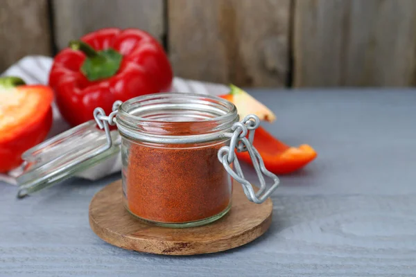 stock image Jar with aromatic paprika powder and fresh bell peppers on grey wooden table