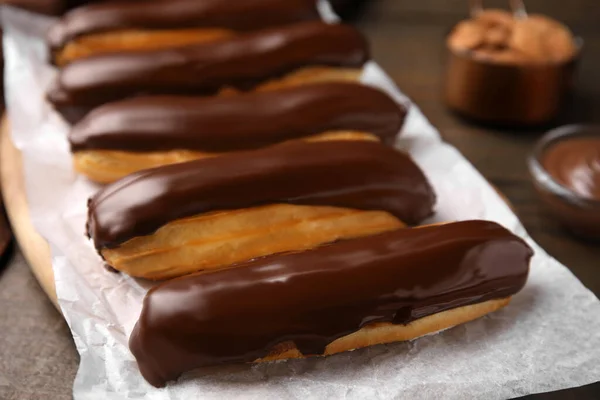 stock image Delicious eclairs covered with chocolate on wooden table, closeup