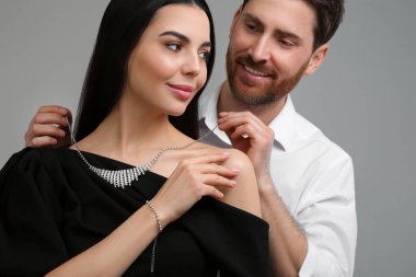 Güzel bir kadına zarif bir kolye takan adam gri arka plana karşı, yakın plan.