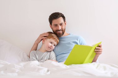 Father reading book with his child on bed at home