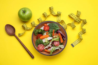 Ölçüm bandı, sebze salatası ve sarı arka planda elma, düz yatak. Kilo verme konsepti
