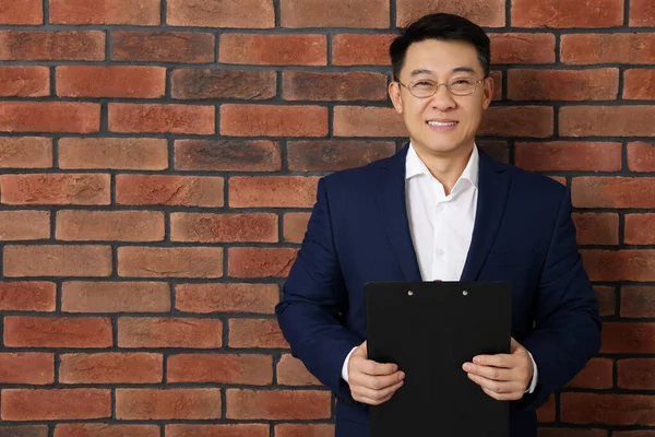 Happy boss with clipboard near brick wall. Space for text