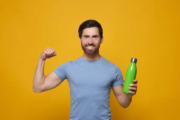 緑色の熱ボトルを持つ男はオレンジの背景に腕を示す — ストック写真