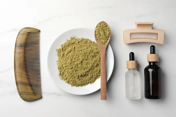 Flat lay composition with henna powder and comb on white marble table. Hair care products