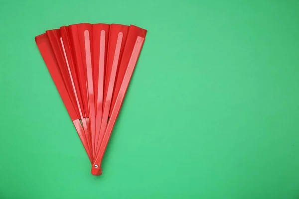 Bright red hand fan on green background, top view. Space for text