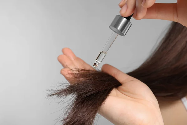 ライトグレーの背景に髪にエッセンシャルオイルを適用する女性 クローズアップ — ストック写真