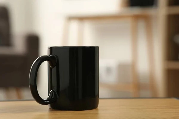 Black mug on wooden table indoors. Mockup for design