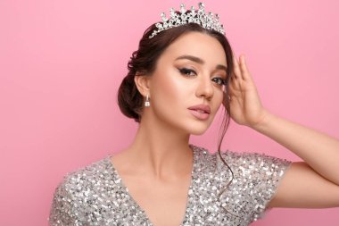 Pembe arka planda lüks bir taç takan güzel bir genç kadın.