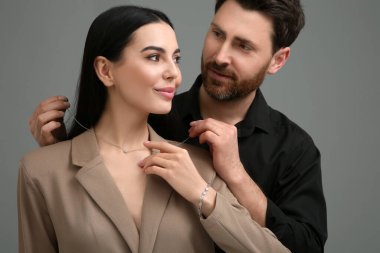 Koyu gri arka planda güzel bir kadına zarif bir kolye takan adam.