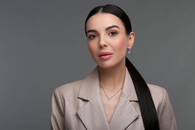 Koyu gri arka planda zarif mücevherleri olan güzel bir genç kadın.