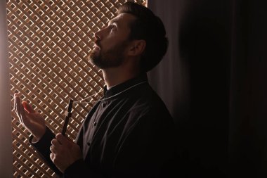 Cüppeli Katolik rahip haç tutuyor ve günah çıkarırken Tanrı 'ya dua ediyor.