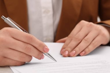 Woman signing document at table, closeup view