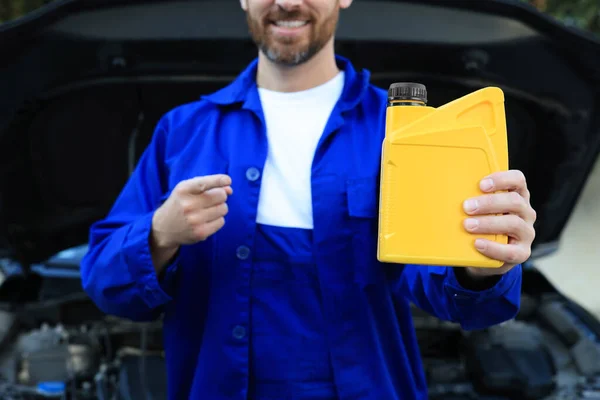 Worker pointing at yellow container of motor oil near car outdoors, closeup