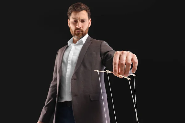Man in suit pulling strings of puppet on black background, low angle view