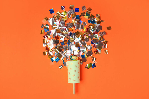 Party popper and colorful confetti on orange background, flat lay