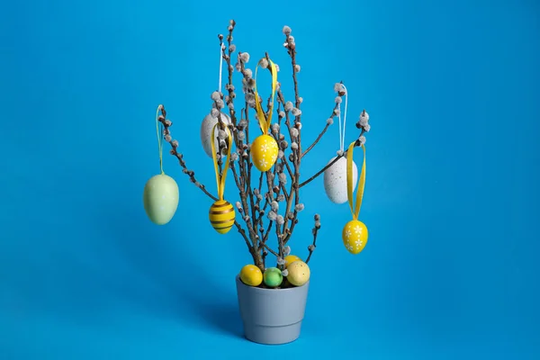 stock image Beautiful willow branches with painted eggs in pot on light blue background. Easter decor