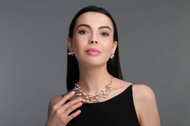 Koyu gri arka planda zarif mücevherleri olan güzel bir genç kadın.