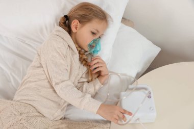 Küçük kız yatakta nefes almak için nebulizör kullanıyor.
