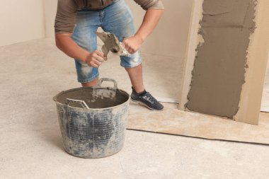 İşçi spatulaya yapıştırıcı sürüyor. Kapalı alanda fayansların yanında, yakın plan.