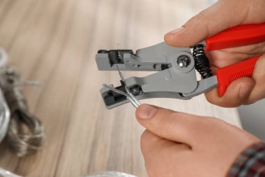 Professional electrician stripping wiring at wooden table, closeup
