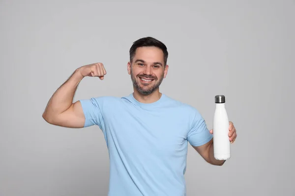 Hombre Feliz Sosteniendo Botella Termo Mostrando Brazo Sobre Fondo Gris —  Fotos de Stock