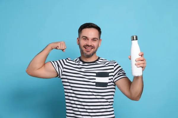 Hombre Feliz Sosteniendo Botella Termo Mostrando Brazo Sobre Fondo Azul —  Fotos de Stock