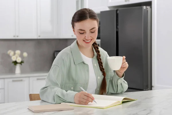 Glückliche Junge Frau Mit Kaffeetasse Notizbuch Weißem Marmortisch Drinnen — Stockfoto