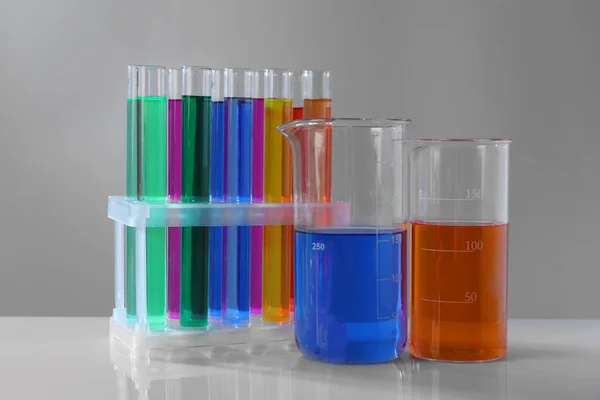 灰色の背景に白いテーブルの上にカラフルな液体を持つ異なる研究室のガラス製品 — ストック写真