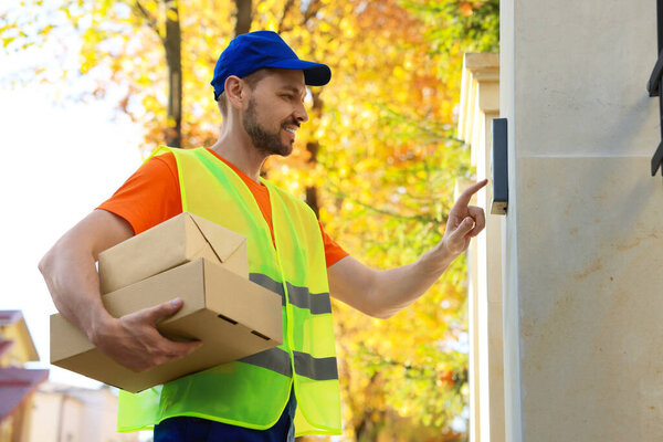 Courier in uniform with parcels ringing doorbell outdoors