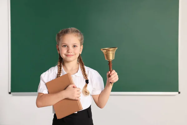 Pupil with school bell near chalkboard in classroom, space for text