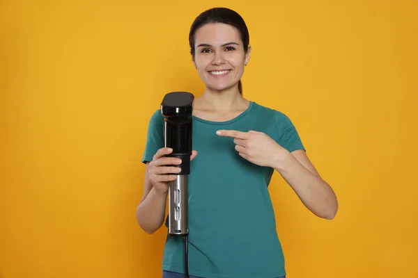 stock image Beautiful young woman pointing on sous vide cooker against orange background