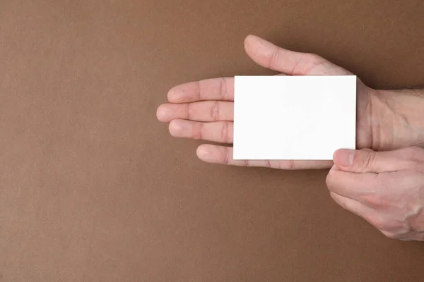 Man holding paper card on brown background, top view. Mockup for design