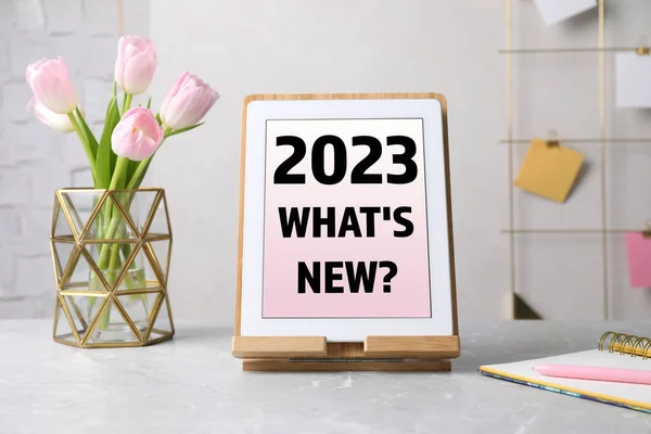 Future trends. 2023 What\'s New? text on tablet display. Modern gadget, flowers and stationery on table