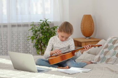 Küçük kız evde internet müzik kursuyla gitar çalmayı öğreniyor. Hobi zamanı.