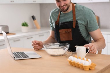 Mutfaktaki ahşap masada çevrimiçi video ile yemek yapmayı öğrenen adam, yakın plan. Hobi zamanı.