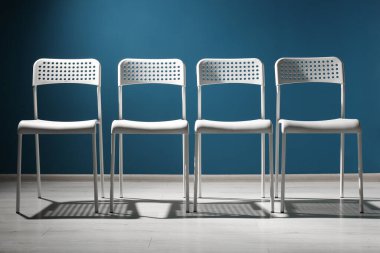 Mavi duvarın yanındaki beyaz sandalyeler. Asker arama çalışanı