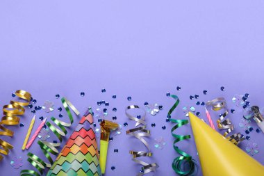 Doğum günü kutlaması. Parti şapkaları, üfleme makinesi, mumlar ve mor arka planda dekoratif aksesuarlar. Metin için boşluk