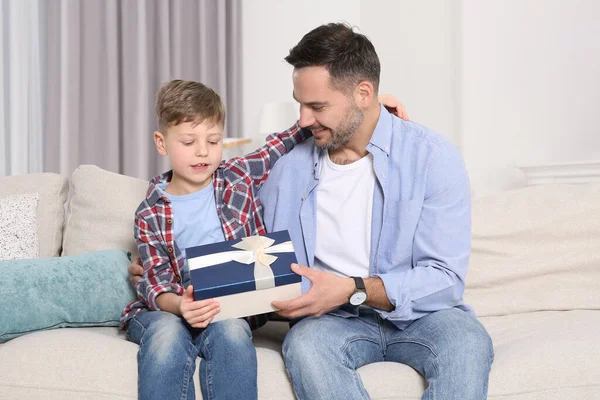 stock image Cute little boy presenting his father with gift on sofa at home