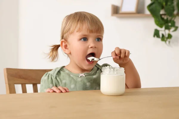 可爱的小孩在屋里用勺子在木桌边吃美味的酸奶 — 图库照片