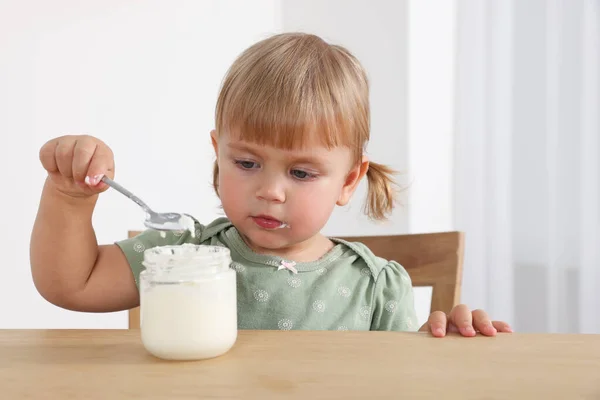 可爱的小孩在屋里用勺子在木桌边吃美味的酸奶 — 图库照片