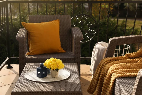 Orange pillow, soft blanket and yellow chrysanthemum flowers on rattan garden furniture outdoors