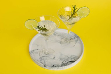 Limon dilimleri ve sarı arka planda biberiyeli martini bardakları.