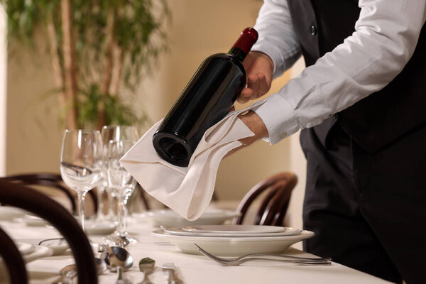 Butler holding bottle of wine near table in restaurant, closeup