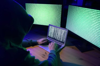 Hacker içerideki ahşap masada bilgisayarlarla çalışıyor. Siber saldırı