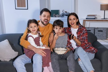 Akşamları evde film izleyen bir aile. Annem uzaktan kumandayla televizyon kanallarını değiştiriyor.