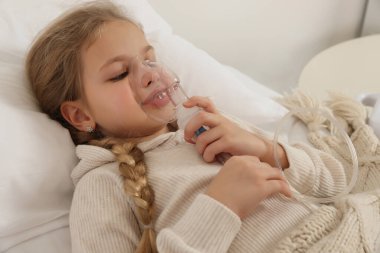 Küçük kız yatakta nefes almak için nebulizör kullanıyor.