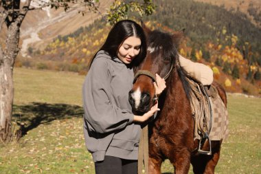 Young woman hugging horse in mountains on sunny day. Beautiful pet