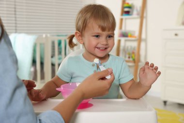 Mother feeding her cute little child with yogurt at home